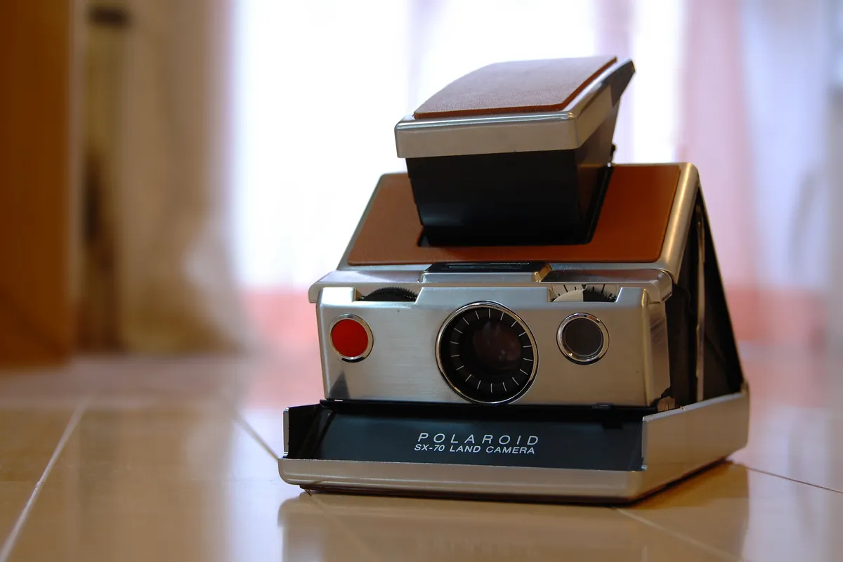 Polaroid SX-70: a chrome and tan leather Polaroid SX-70, unfolded, on a tiled floor